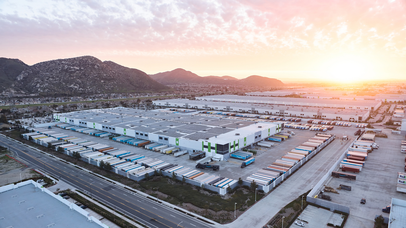 Aerial view of an Amazon fulfillment center at sunrise, with trailers lined up at the loading docks