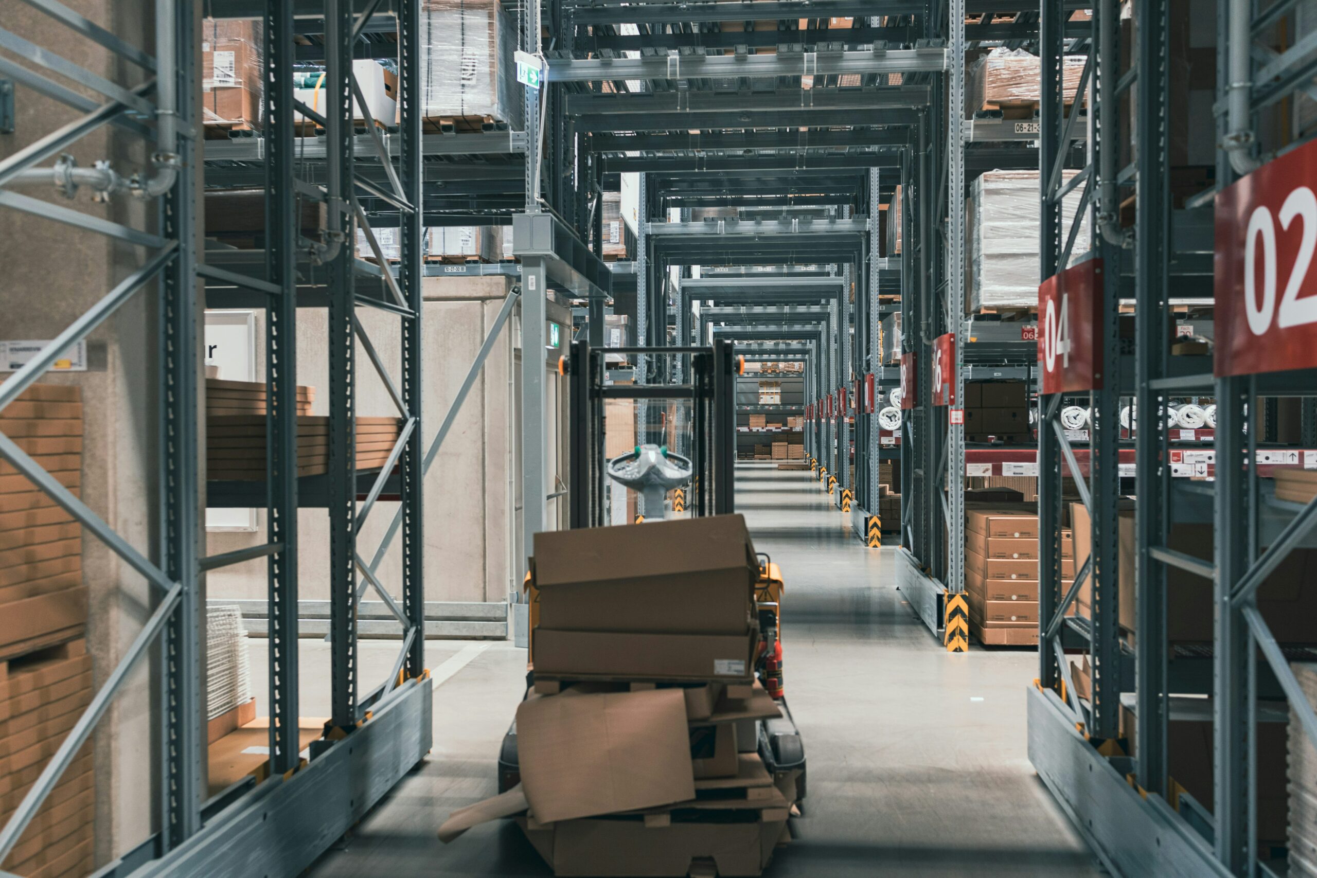Warehouse aisle with numbered racking bays and a pallet of flat-packed cartons
