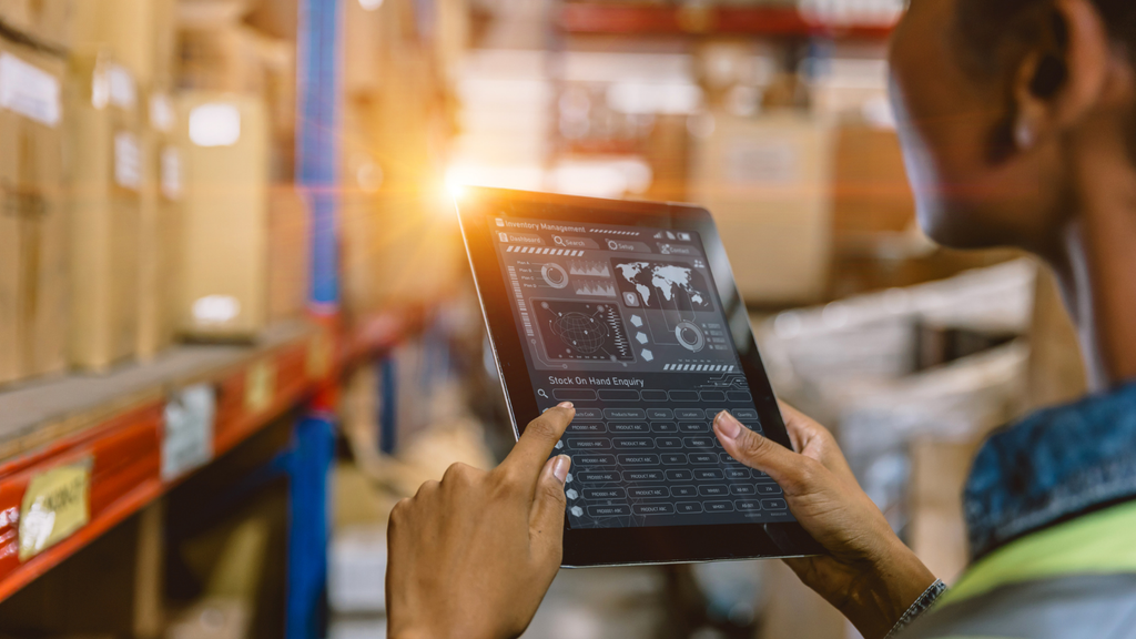 Warehouse management system showing a worker using a digital tablet to manage inventory and warehouse operations