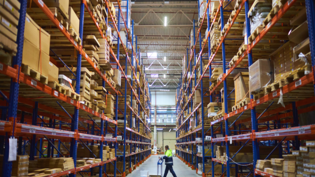 Large warehouse with storage racks and a worker managing inventory and physical warehouse operations