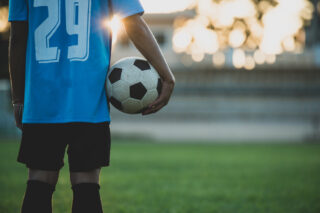 Niño en posición de descanso sosteniendo un balón de fútbol en el lado derecho del cuerpo